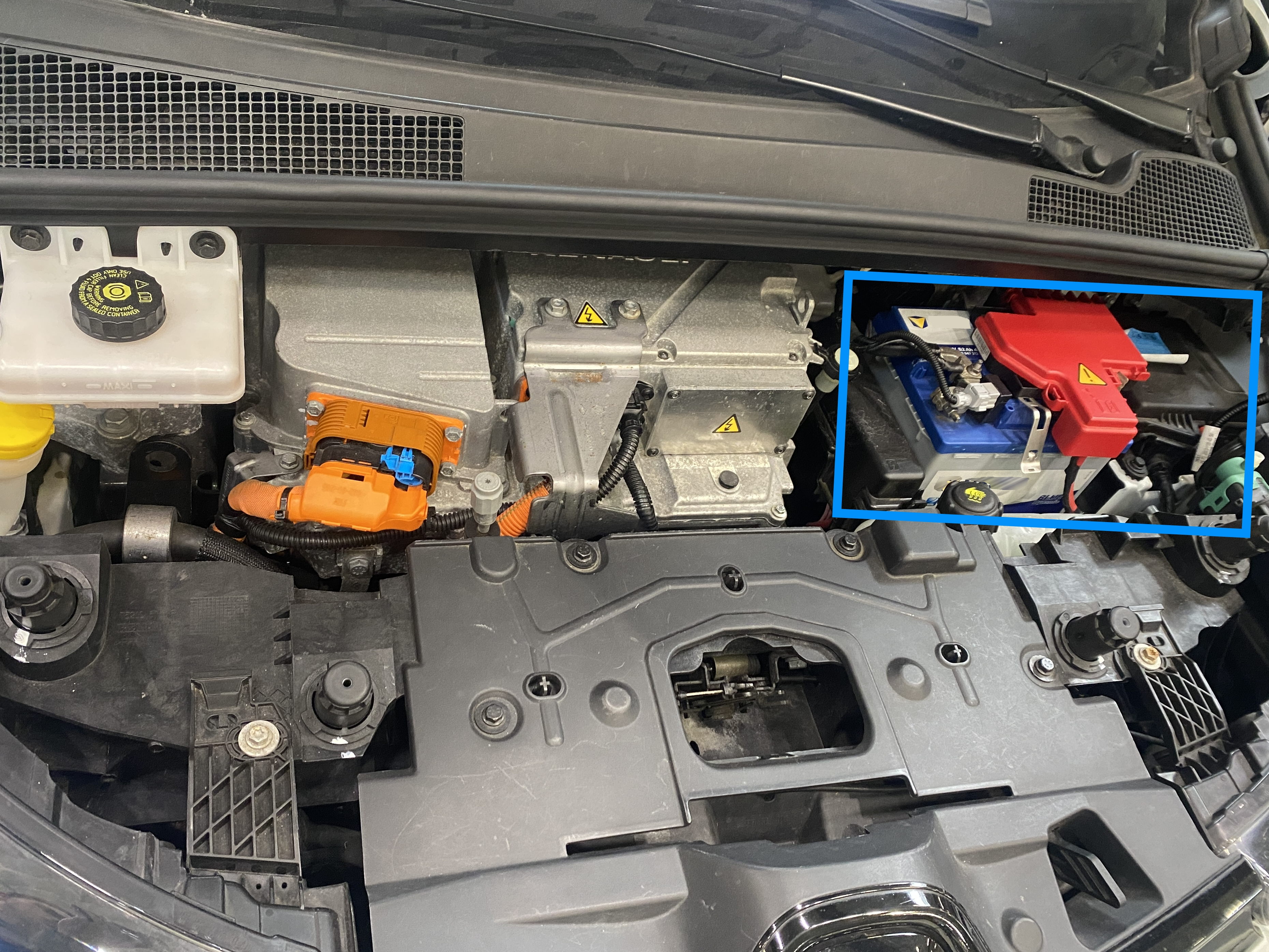 Motorraum eines Elektrofahrzeugs mit sichtbaren Hochvoltkomponenten und hervorgehobener 12-Volt-Batterie, die das Niedervolt-Bordnetz für Steuergeräte und Komfortfunktionen versorgt.